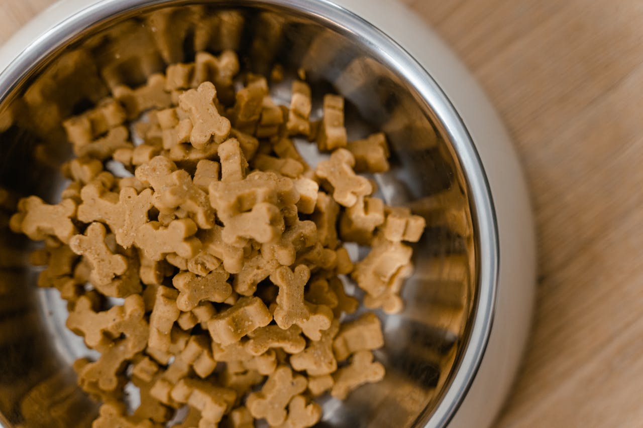 services-04 A close-up view of dog bone-shaped biscuits in a stainless steel bowl on a wooden surface.